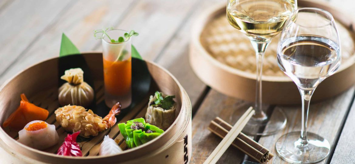 Several different traditional Chinese dimsum dumplings in a wooden basket cooked for guests on a wooden table in a restaurant.