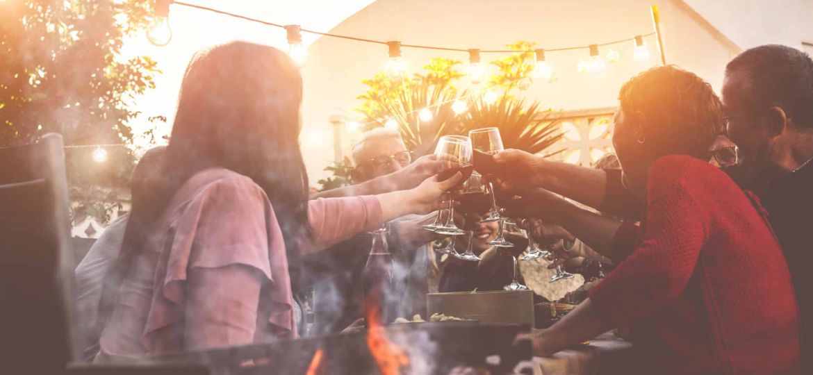 Happy trendy family cheering with red wine at barbecue dinner ou